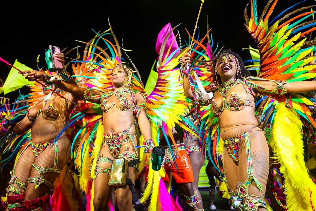 A line of masqueraders in rainbow feathered wings dancing under stage lights at night
