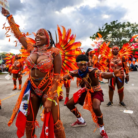 A masquerader in orange feathers holding a flag aloft